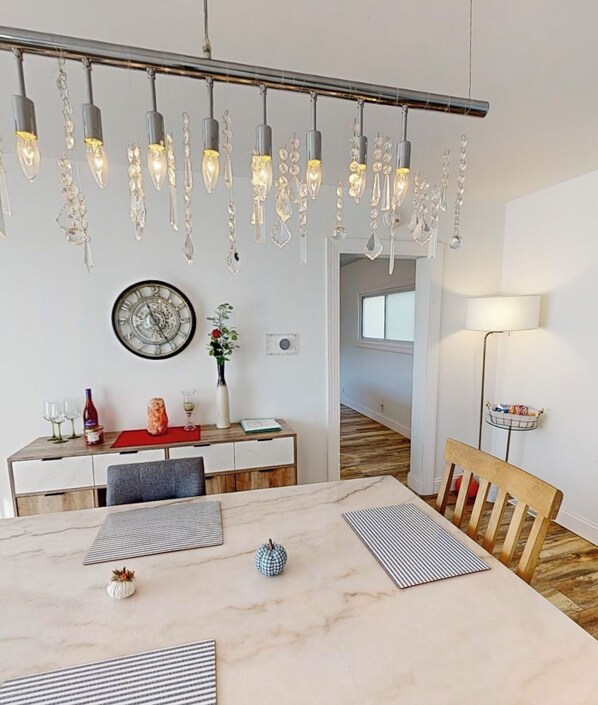 A dining area with a marble table, hanging light fixtures, a clock, and a vase with flowers.