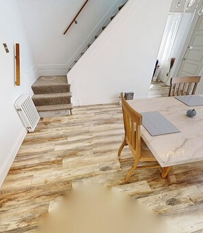 A dining area with a marble table and wooden chairs, a staircase with carpeted steps, and a radiator on the wall.