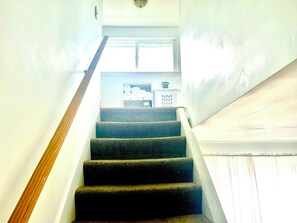 Eine Treppe mit Geländer führt zu einer Zwischenebene mit einem Fenster und einem Regal mit gefalteten Gegenständen.