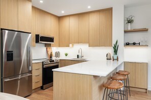 Een moderne keuken met houten kastjes, roestvrijstalen apparatuur, een groot eiland met barkrukken en een inbouwmagnetron.