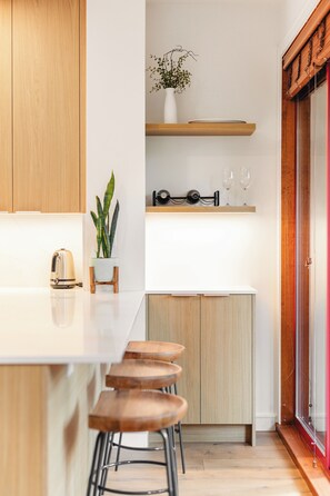 A modern kitchen with wooden cabinets, a white countertop, a plant, a kettle, and a wine rack. - Modern Mountain Retreat, Ski-In, Hot Tub (Whistler)