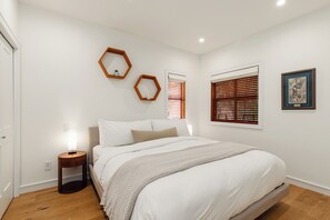 Een slaapkamer met een bed, een nachtkastje, een spiegel aan de muur en een raam met jaloezieën.
