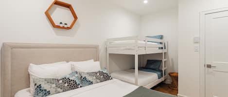 Un dormitorio con una cama litera, una cama individual con almohadas estampadas, un cabecero de madera, un espejo pequeño y una puerta.