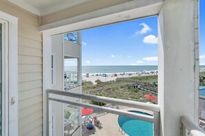 A balcony with a view of a beach, a pool, and a lifeguard stand. - Windy Hill Oceanfront Suite, Pool & Hot Tub (North Myrtle Beach)