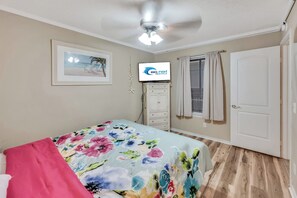 A bedroom with a bed, a ceiling fan, a framed picture, a television, and a door. - Windy Hill Oceanfront Suite, Pool & Hot Tub (North Myrtle Beach)
