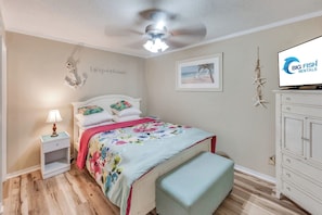 A bedroom with a bed, a nightstand, a lamp, a ceiling fan, a framed picture, a television, and a wardrobe. - Windy Hill Oceanfront Suite, Pool & Hot Tub (North Myrtle Beach)