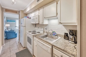 A compact kitchen with white cabinetry, a built-in microwave, a stove, and a sink. - Windy Hill Oceanfront Suite, Pool & Hot Tub (North Myrtle Beach)
