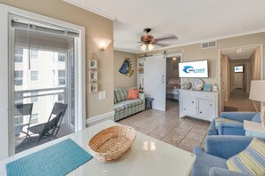 A well-lit living room with a sofa, a dining table with a basket, and a television displaying 'Big Fish Rentals'. - Windy Hill Oceanfront Suite, Pool & Hot Tub (North Myrtle Beach)
