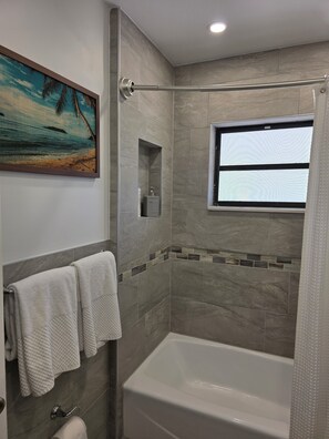 Ein modernes Badezimmer mit einer Badewanne, einer Duschkabine und einem Fenster.
