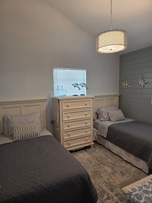 Ein Schlafzimmer mit zwei Betten, einem Schminktisch, einer Hängeleuchte und einem Fenster mit Jalousien.
