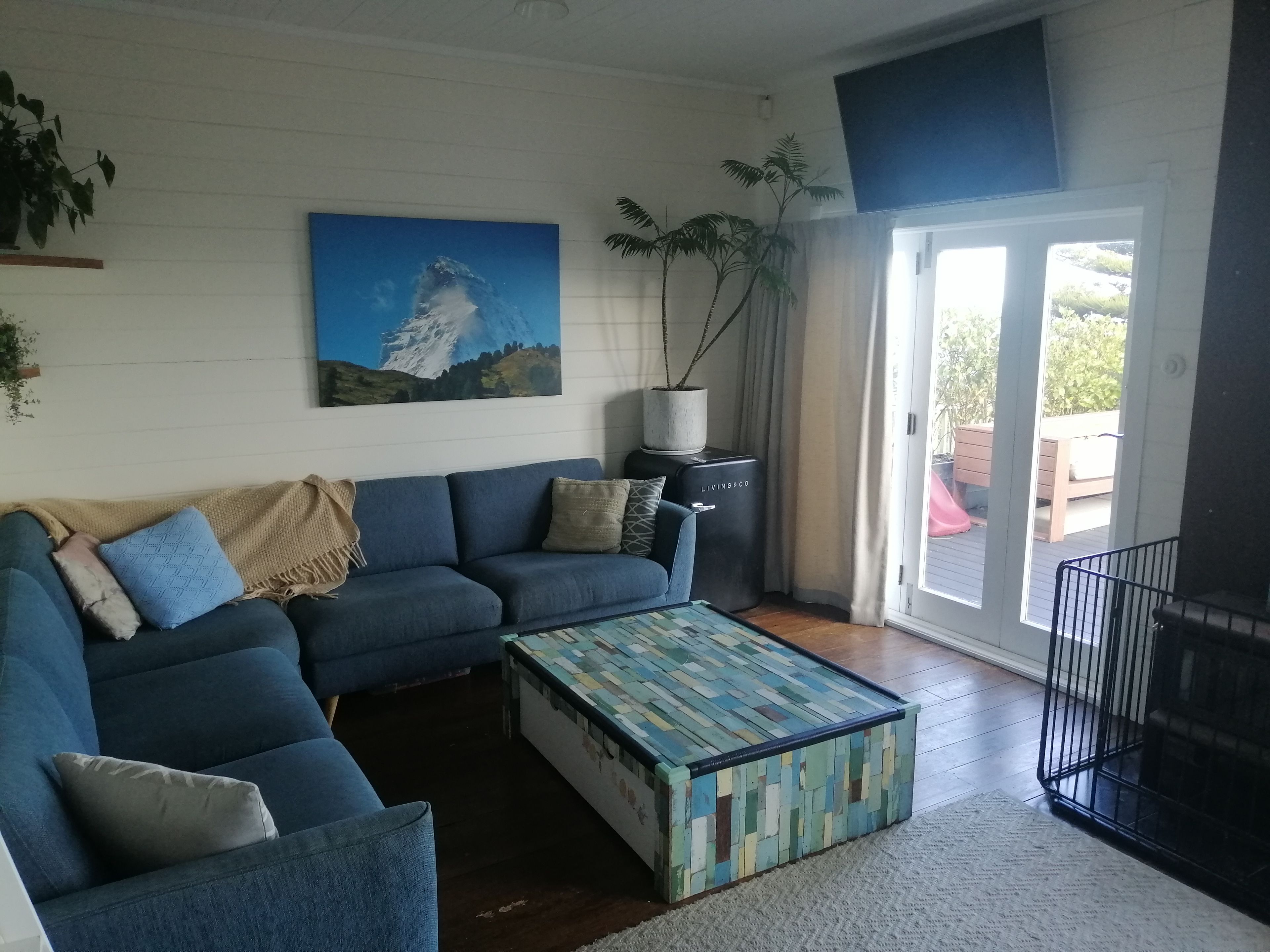 A living room with a blue sofa, a colorful coffee table, and a painting of a mountain.