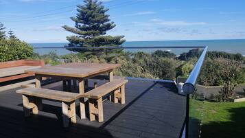 Une terrasse en bois avec une table de pique-nique et des bancs, donnant sur une étendue d’eau.
