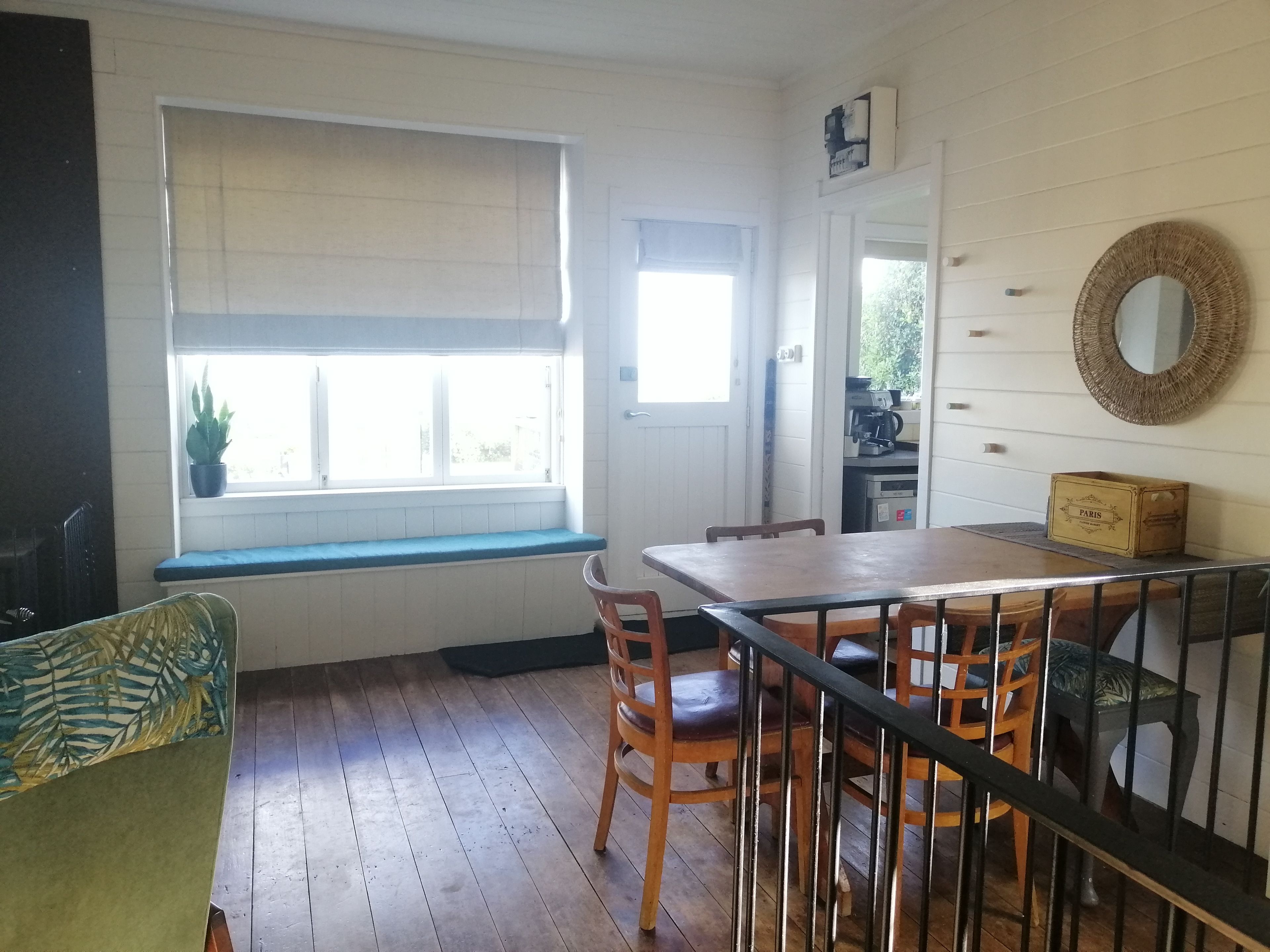 Une pièce comprenant une table à manger en bois, des chaises, un banc, une fenêtre avec des stores, une porte et un miroir fixé au mur.