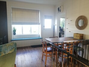 A room with a wooden dining table, chairs, a bench, a window with blinds, a door, and a wall-mounted mirror.