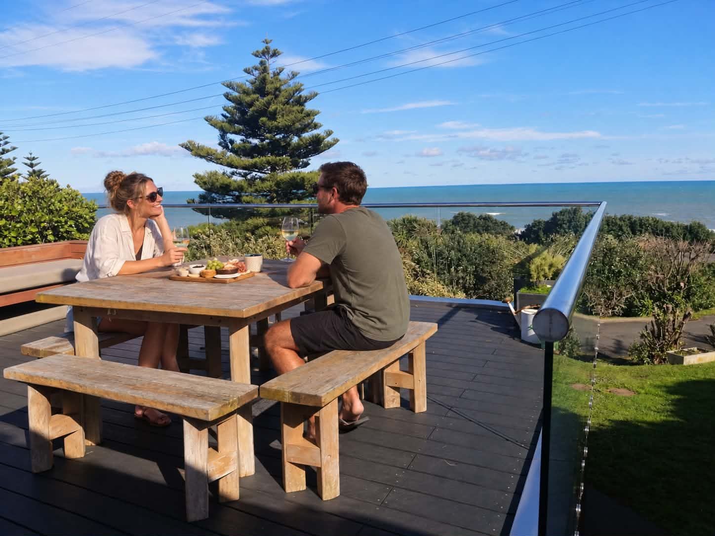 Une terrasse en bois avec une table et des bancs, donnant sur une étendue d’eau et une zone verdoyante.