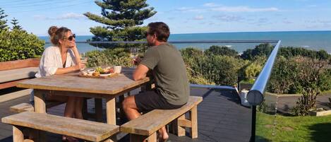 Une terrasse en bois avec une table et des bancs, donnant sur une étendue d’eau et une zone verdoyante.