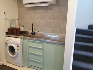 A compact kitchen with a built-in washing machine, a stainless steel sink, and a tiled backsplash.