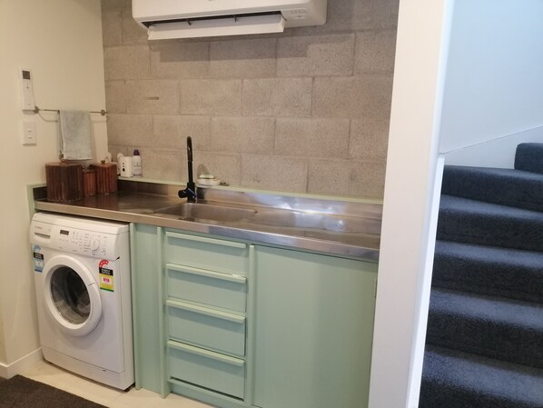 A compact kitchen with a built-in washing machine, a stainless steel sink, and a tiled backsplash.