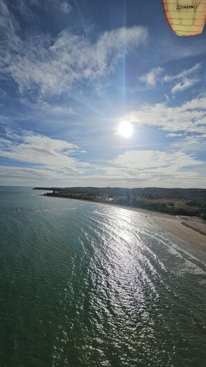 Paisagem costeira com praia, céu claro e reflexo do sol na água.
