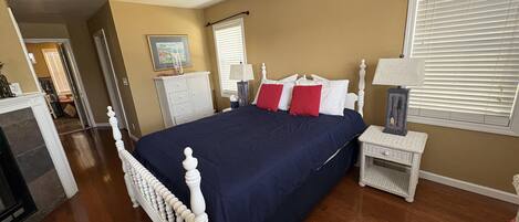 A bedroom with a large bed, a bedside table, a lamp, and a window with blinds.