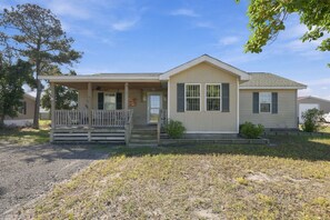 A single-story mobile home with a porch, a front door, and a small front yard. - Nook Hill | 3-bedroom, Pool, Dog-Friendly (Harkers Island)