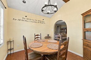 Un coin repas avec une table ronde en bois, quatre chaises, un lustre et un mur sur lequel est inscrit un message de remerciement.