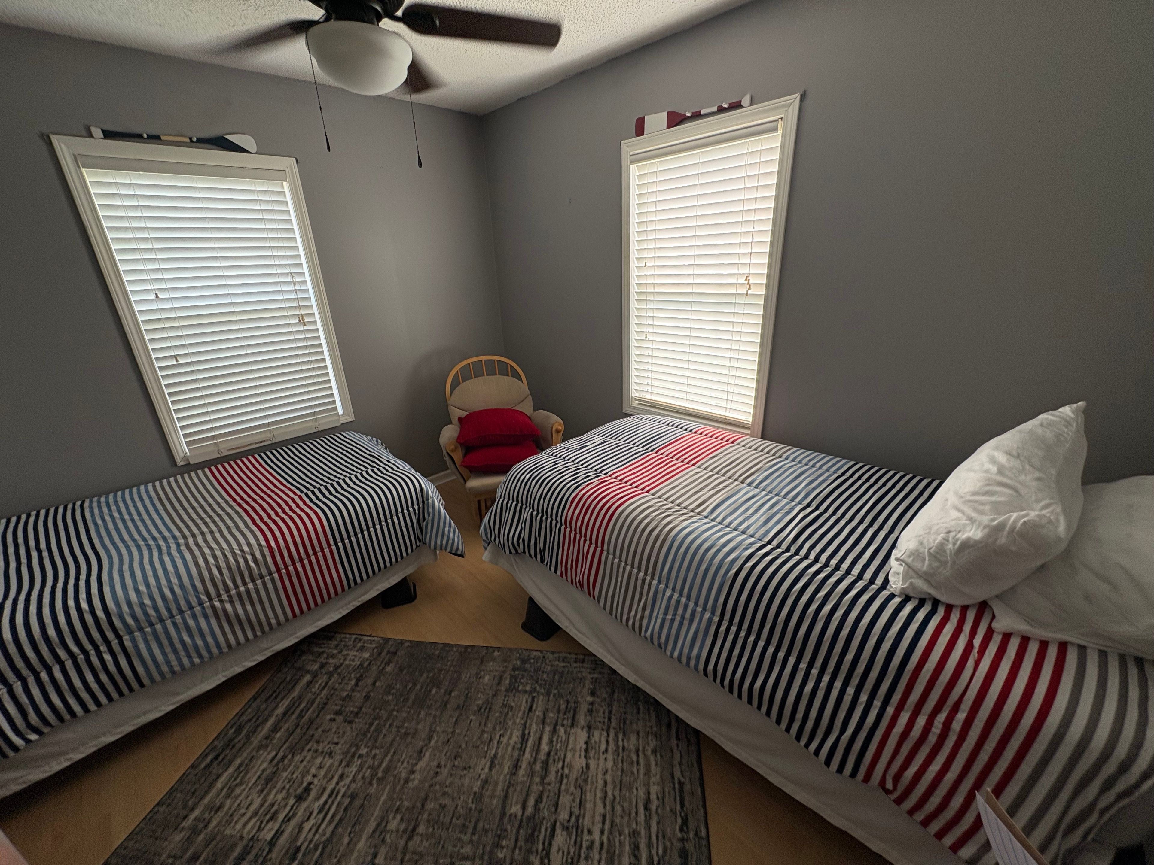 Una camera da letto con due letti singoli, una sedia e una ventola a soffitto.
