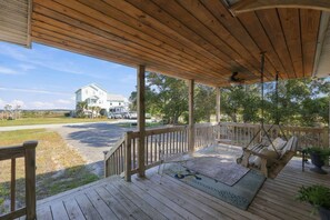 Une terrasse en bois avec une chaise suspendue et un banc, donnant sur une pelouse avec une maison en arrière-plan.