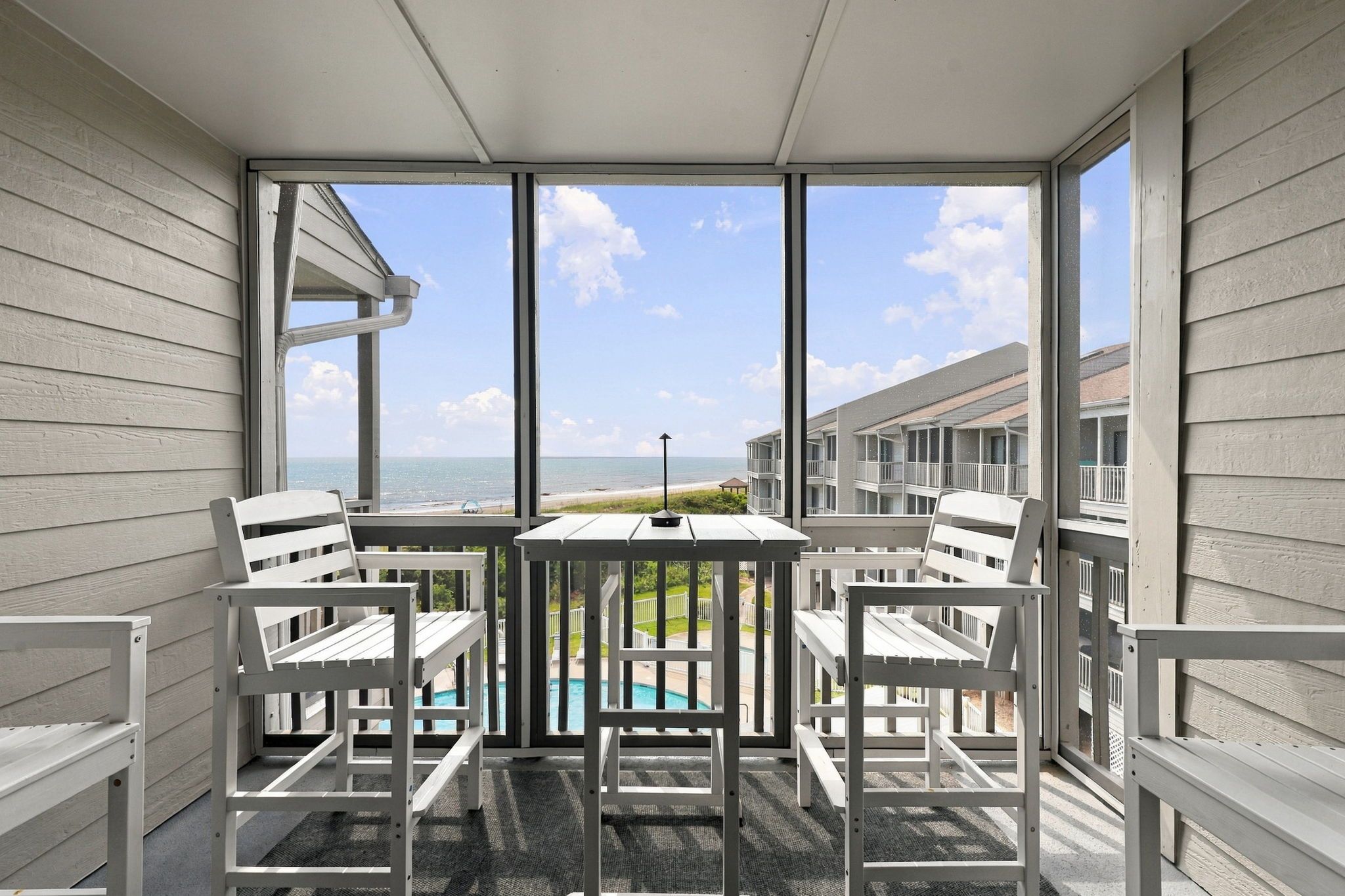 Ein Balkon mit Blick auf einen Pool und den Ozean, ausgestattet mit weißen Stühlen und einem Tisch.