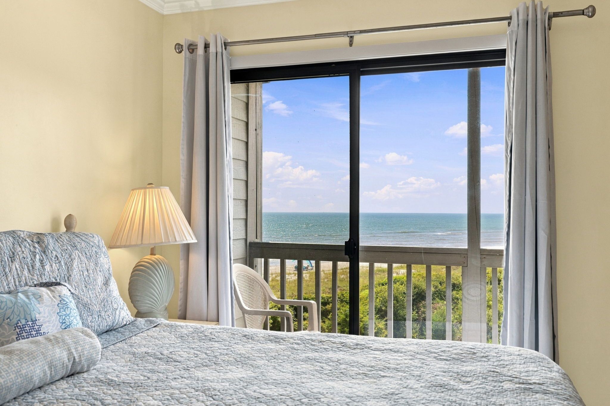 A bedroom with a view of the sea, a bed, a chair, and a lamp.