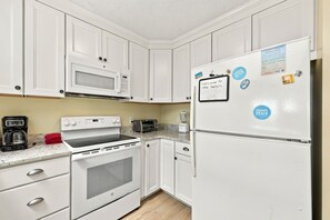 A kitchen with white cabinets, a microwave, a stove, a toaster, and a refrigerator with magnets. - Pack the Flip‑Flops — Family Fun Starts Here (Atlantic Beach)