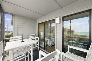 A balcony with a table and chairs, a glass door leading to an indoor area, and a view of the beach. - Pack the Flip‑Flops — Family Fun Starts Here (Atlantic Beach)