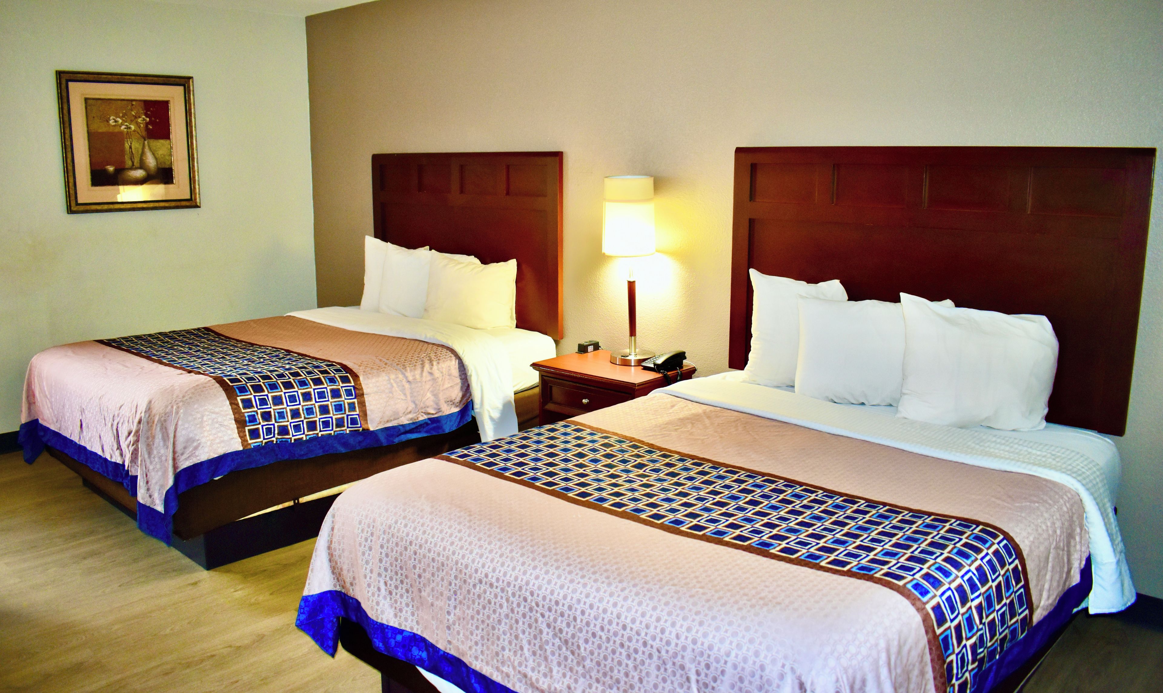 Habitación de hotel con dos camas, una mesita de noche con lámpara y un cuadro en la pared.
