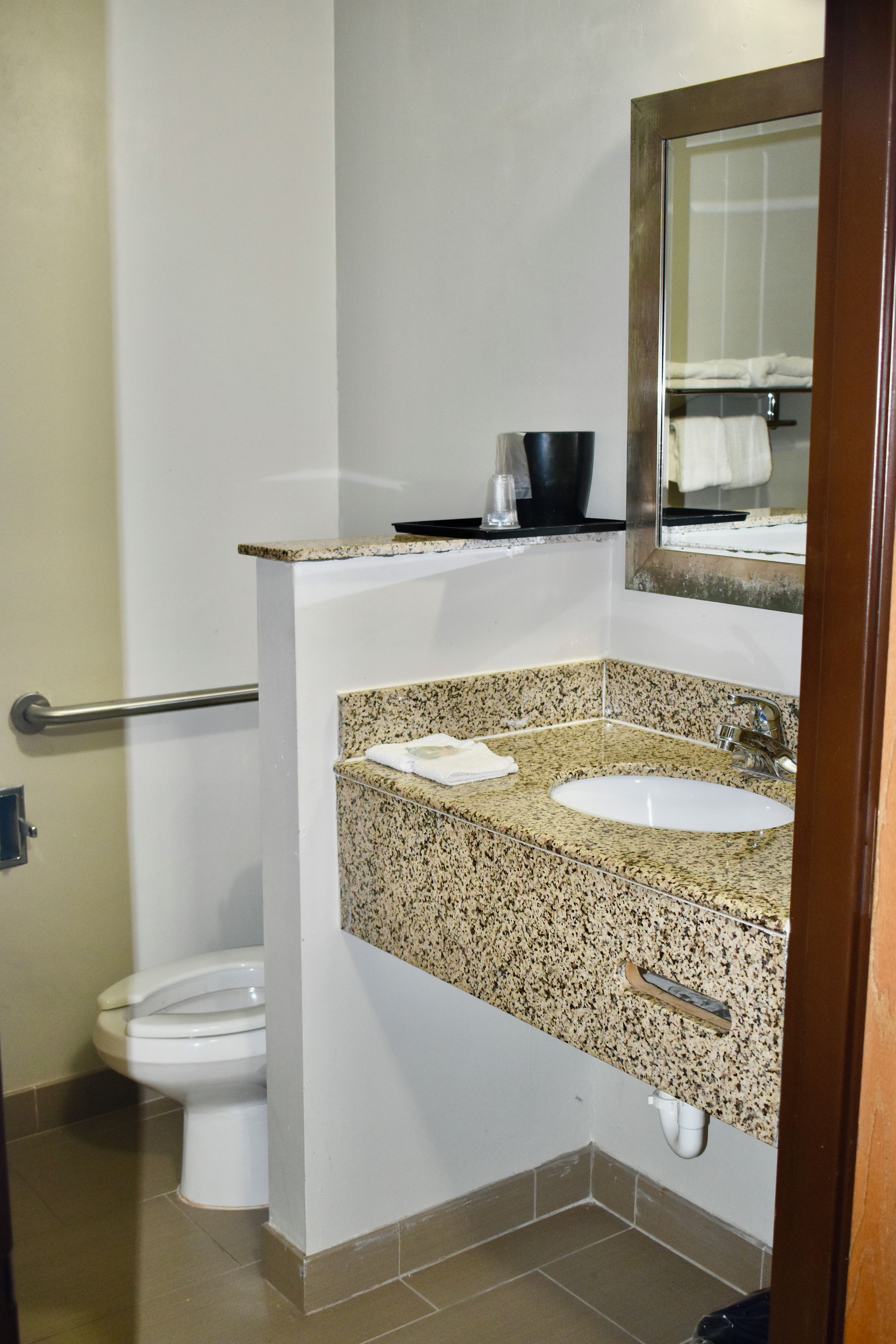 Une salle de bain avec des toilettes blanches, un lavabo sur un plan de travail en granit, un miroir et un porte-serviettes.