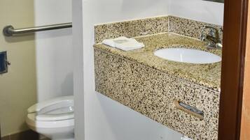 Une salle de bain avec des toilettes blanches, un lavabo sur un plan de travail en granit, un miroir et un porte-serviettes.