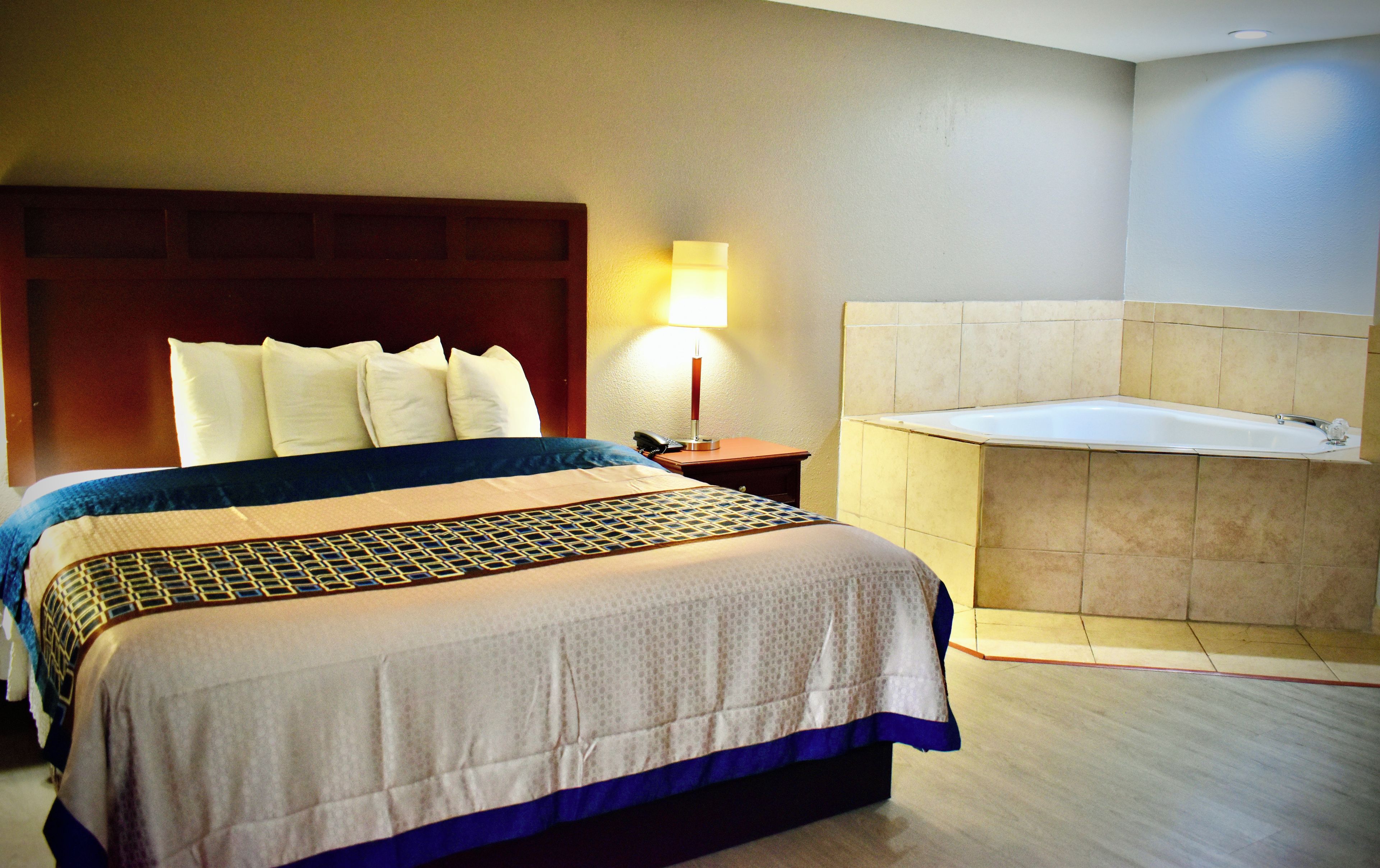 A hotel room with a large bed, a bedside lamp, a telephone, and a bathtub.