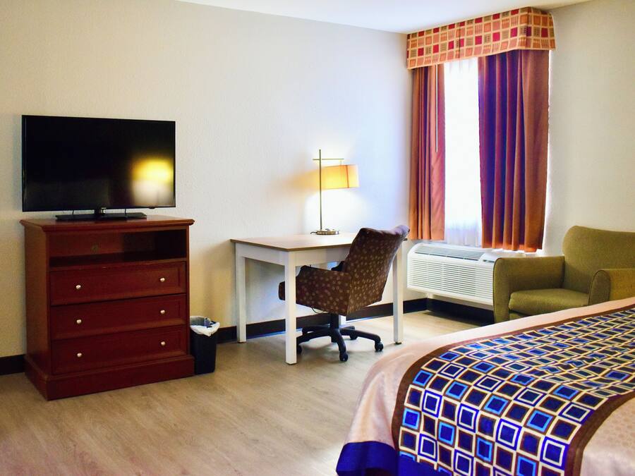 A hotel room with a TV, a desk, a chair, a bed, and a window with curtains.