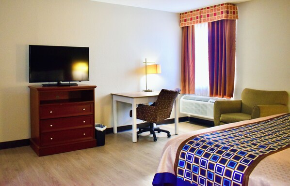 A hotel room with a TV, a desk, a chair, a bed, and a window with curtains. - EXPRESS INN & SUITES SOUTH LITTLE ROCK (Little Rock)