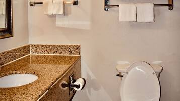 Un baño con lavamanos de encimera de granito, inodoro y perchero para toallas.