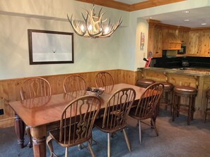 A dining area with a wooden table and chairs, a chandelier, and a kitchen area with wooden cabinets and a bar. - Beaver Creek Slopeside - True ski in/ ski out  3-bedroom condo (Beaver Creek)