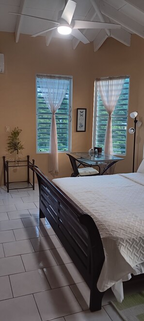 A bedroom with a bed, a table, and two windows with curtains. - Sun-lit Arched Styled Villa with Scenic Mountain Views and Cool Tranquil Breeze (charlotte amalie)