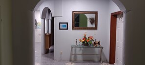 A hallway with a glass console table displaying a floral arrangement, a framed mirror, and a framed certificate on the wall. - Sun-lit Arched Styled Villa with Scenic Mountain Views and Cool Tranquil Breeze (charlotte amalie)