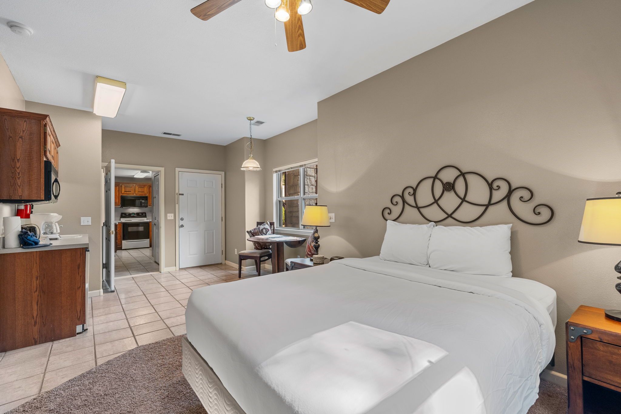 Une chambre d’hôtel avec un grand lit, un bureau, une chaise, une lampe et un ventilateur de plafond.