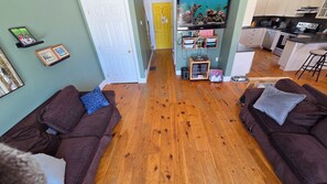 Ein Wohnzimmer mit zwei braunen Sofas, Holzboden, einer Küchenzeile mit modernen Geräten und einem Aquarium.