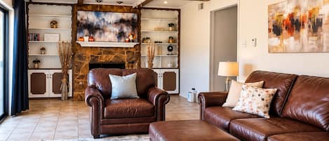 Una sala de estar con chimenea, sofás de cuero, una mesa de centro y una estantería.