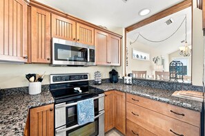 A kitchen with wooden cabinets, a stainless steel microwave, a black stove, and granite countertops. - Beach Bungalow: Soundside, Hot Tub, Sound Views, Village Beach Club Access (Nags Head)