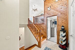 A wooden staircase leading to a second floor with a ceiling fan and decorative wall art. - Beach Bungalow: Soundside, Hot Tub, Sound Views, Village Beach Club Access (Nags Head)