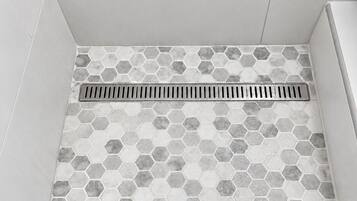 Casa de banho com azulejos de padrão hexagonal e ralo visível.
