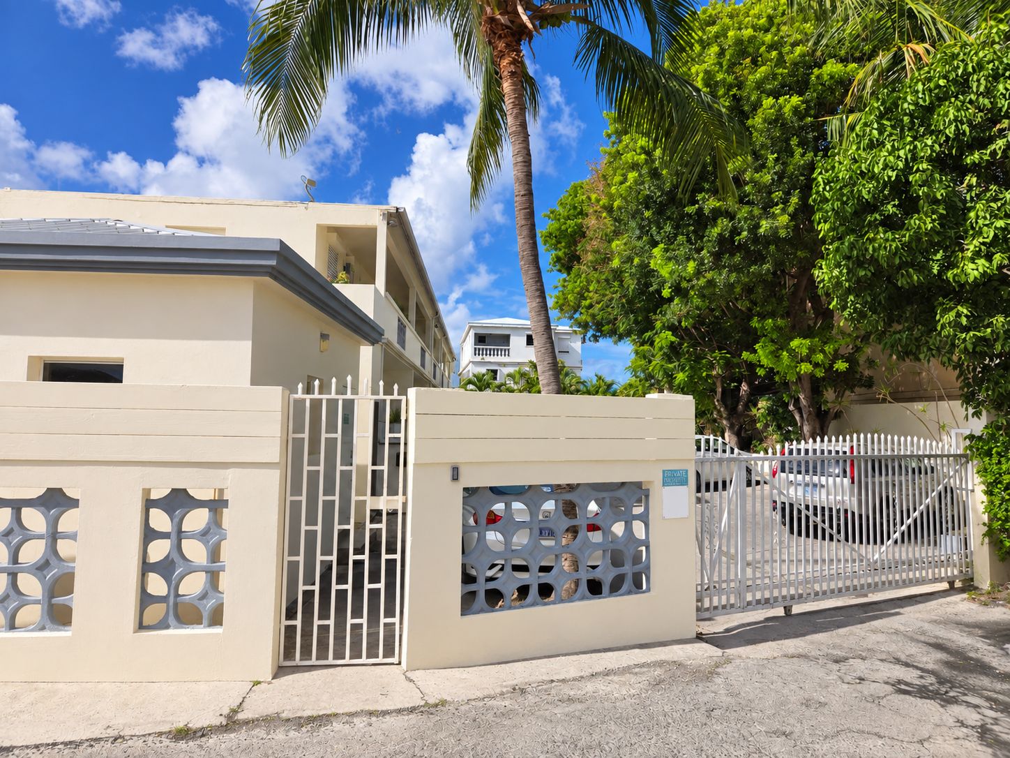 A gated residential area with a beige building, a white fence, and a palm tree.