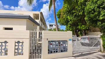 A gated residential area with a beige building, a white fence, and a palm tree.